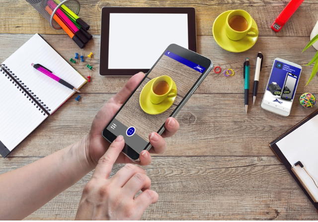 A person using a smartphone to take a picture of a cup of coffee.